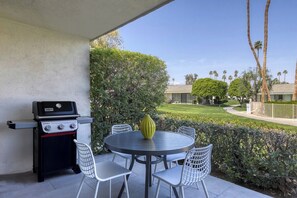 Eine Terrasse im Freien mit Grill, rundem Tisch und Stühlen.