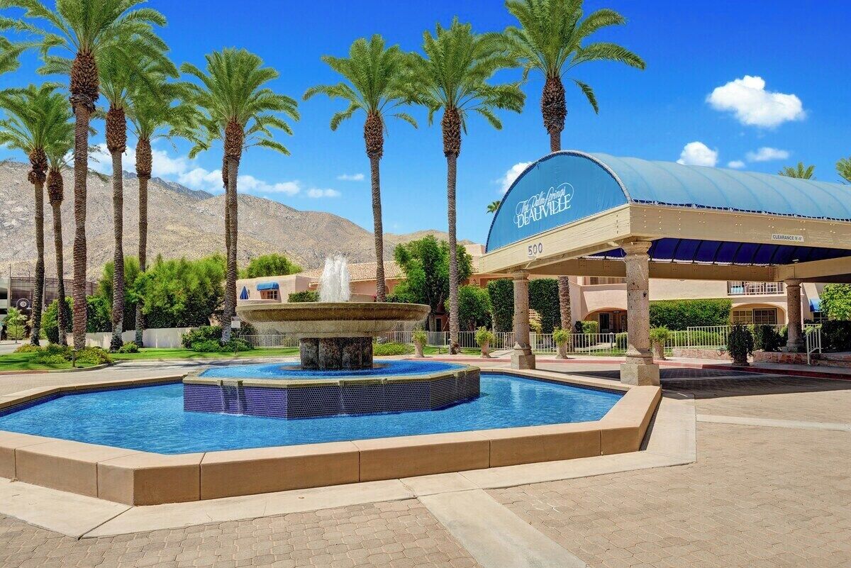 A hotel with a pool, palm trees, and a mountain in the background.