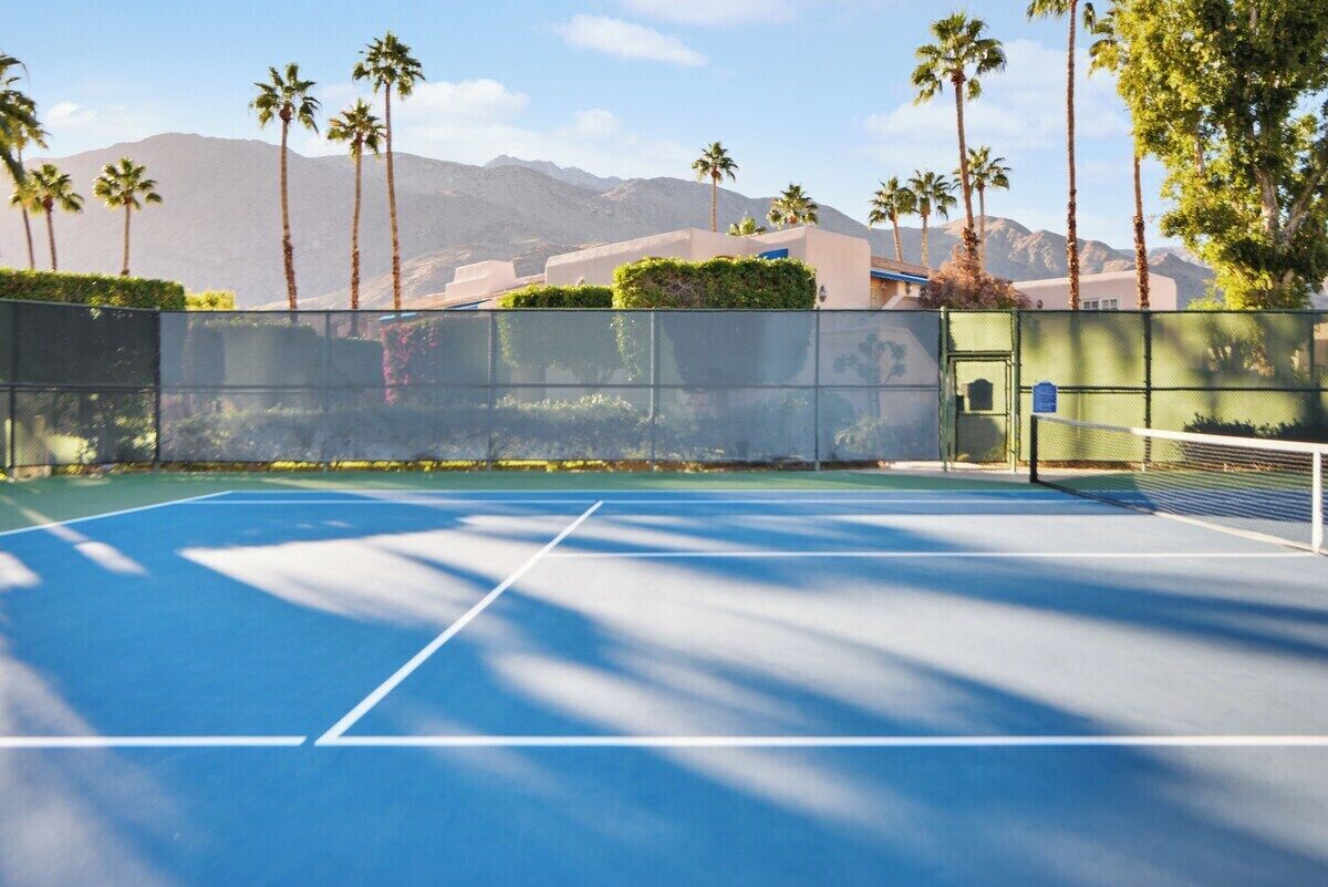Una cancha de tenis al aire libre con vistas despejadas a montañas y palmeras al fondo.