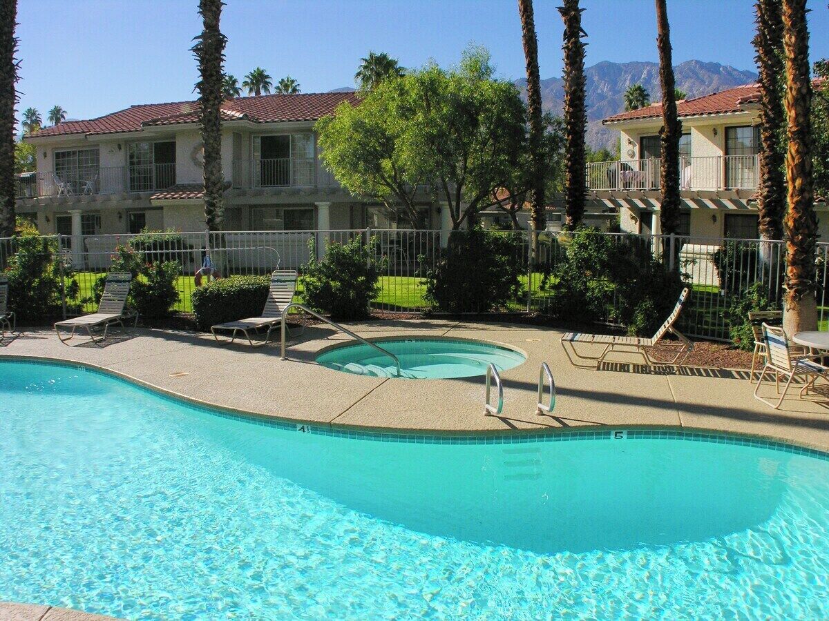 A swimming pool with a clear blue water, surrounded by lounge chairs and a small hot tub.