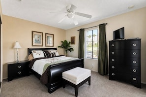 A bedroom with a bed, a dresser, a television, a ceiling fan, and a window with curtains. - Mesquite Serenity Phase 4 (Palm Springs)