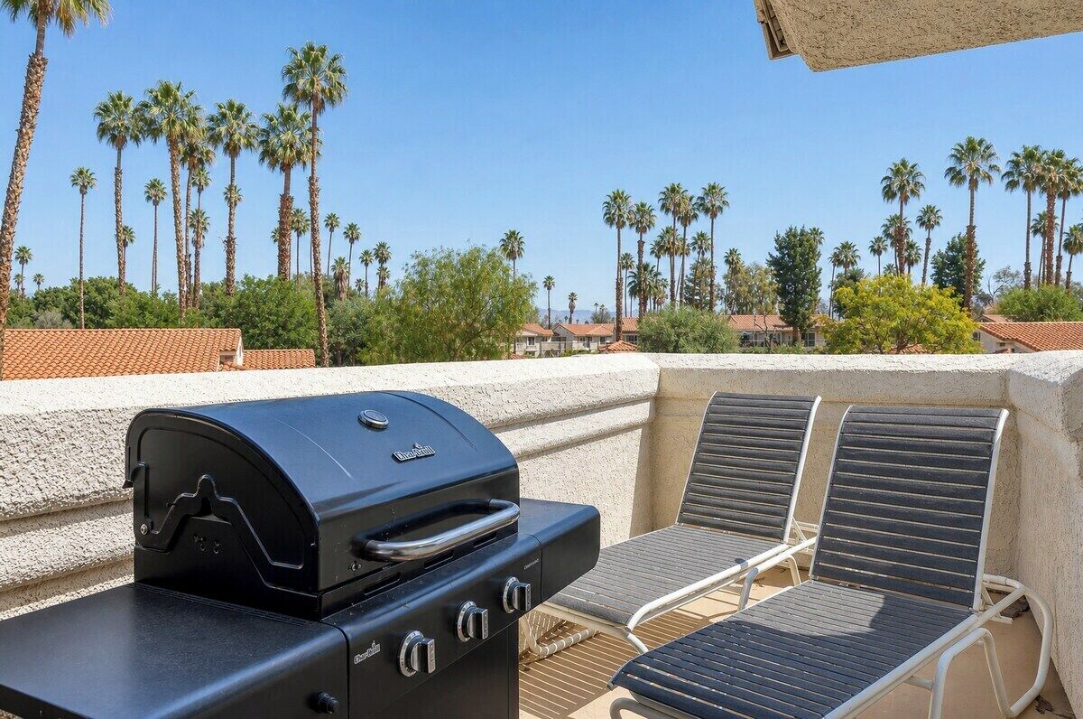 Un barbecue, deux chaises longues et une vue sur des palmiers et des maisons.