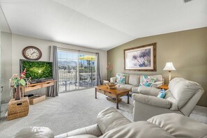 A living room with a flat-screen TV, a sofa set, a coffee table, and a balcony with a view. - Mesquite Breeze Phase 1 (Palm Springs)
