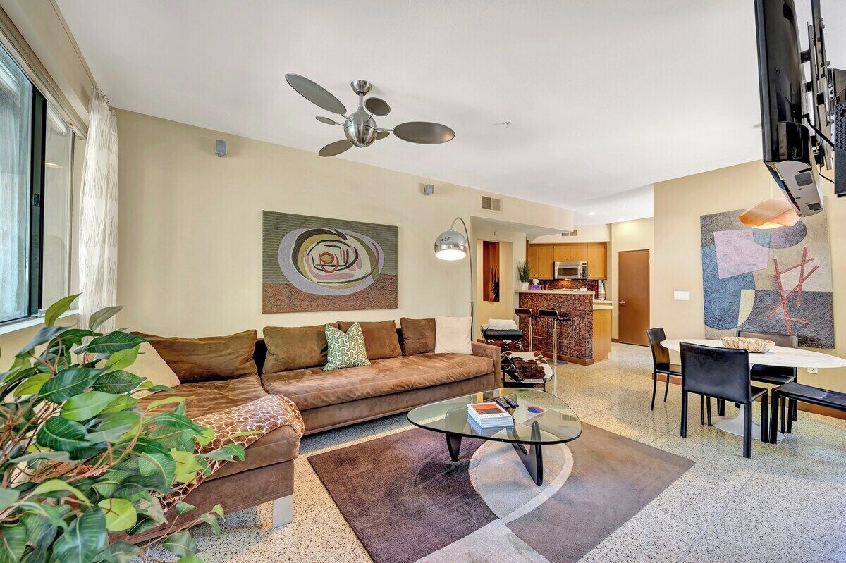 A modern living room with a brown sofa, a glass coffee table, and a ceiling fan.