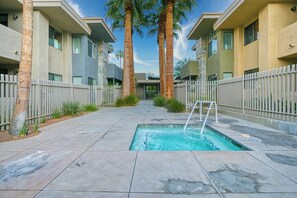 A swimming pool with a ladder, surrounded by a fence, and palm trees in a courtyard with apartment buildings. - Biltmore Chic - South Palm Springs (Palm Springs)