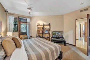 Un dormitorio con una cama, televisor, estantería y una puerta que da a otra habitación.