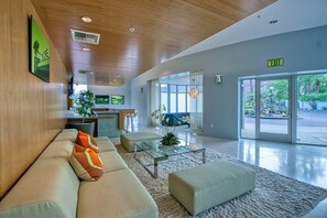 A modern lobby with a sofa, ottoman, glass coffee table, and a reception desk. - Biltmore Chic - South Palm Springs (Palm Springs)