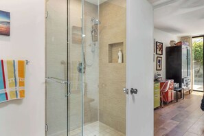 Een moderne badkamer met een douchecabine van glas, een houten wastafelmeubel met spiegel en een klein plankje met toiletartikelen.