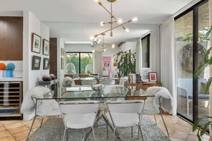 Een moderne eethoek met een glazen tafel, witte stoelen en een kroonluchter.