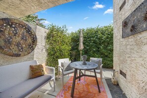 Eine Terrasse im Freien mit einem runden Tisch, zwei Stühlen, einer Couch und einem dekorativen Wandelement.