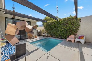 Ein Swimmingpool mit Pergola, Gartenmöbeln und einer Wand, die von Kletterpflanzen überwuchert ist.