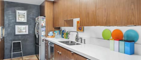 Une cuisine moderne avec des meubles en bois, un plan de travail blanc, un évier en acier inoxydable et un réfrigérateur.