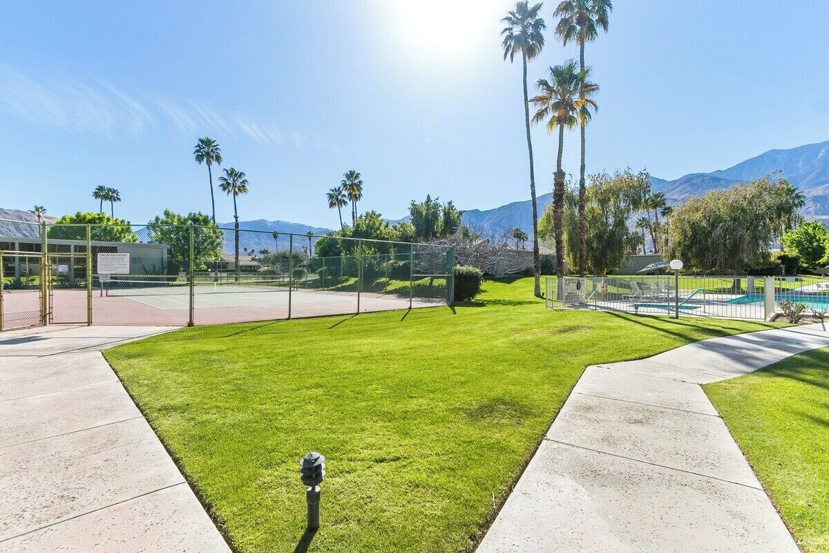 A well-maintained grassy area with a basketball court, a pool, and a mountain backdrop.