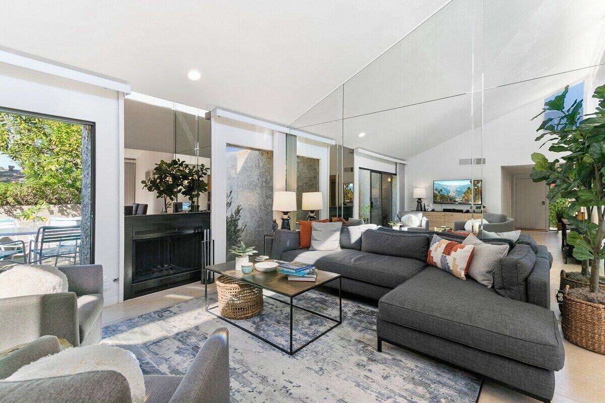 A modern living room with a fireplace, grey sofas, a coffee table, and a large window.