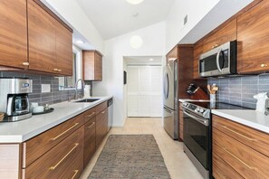 A modern kitchen with wooden cabinets, stainless steel appliances, and a tiled backsplash. - Saddlerock Garden Haven (Palm Springs)