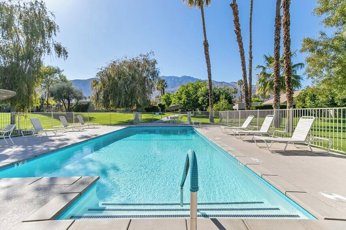 Una piscina rectangular con agua cristalina y azul, rodeada por una terraza pavimentada con sillones de descanso.