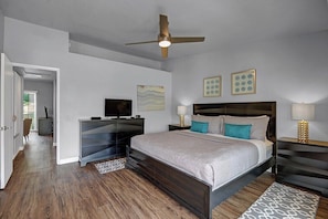 A bedroom with a bed, bedside tables, a ceiling fan, a TV, and artwork on the wall. - Mesquite Desert Bungalow (Palm Springs)