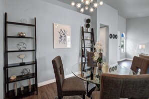 A modern dining area with a glass table and chairs, surrounded by dark wooden shelves with decorative items. - Mesquite Desert Bungalow (Palm Springs)