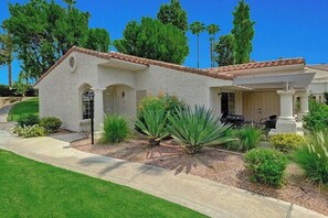 A stucco house with a tiled roof, a covered porch, and a landscaped front yard with agave plants. - Mesquite Desert Bungalow (Palm Springs)