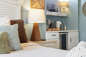 Une chambre d’hôtel comprenant un lit, des oreillers, une table de chevet, une lampe, une petite kitchenette et un miroir.