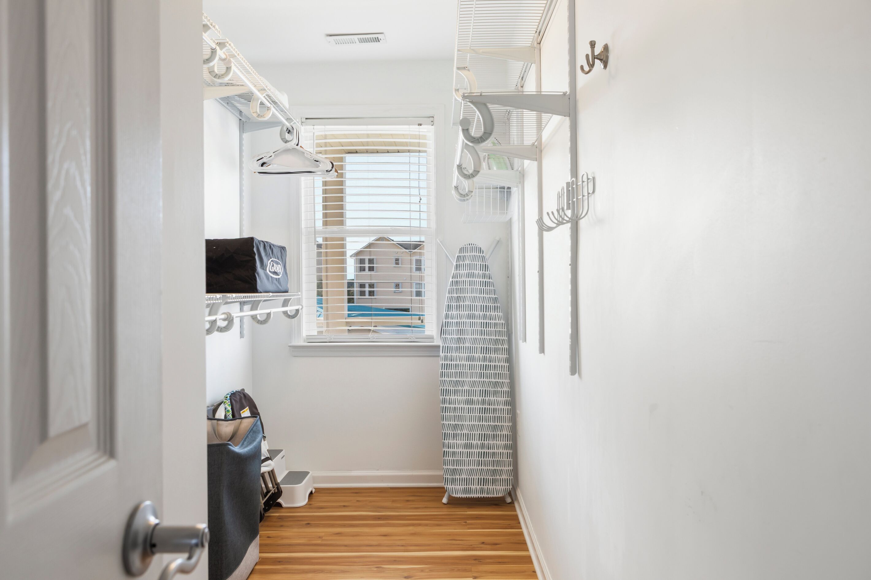 A narrow hallway with a wooden floor, a window with blinds, a radiator, and a white wall with a hook.