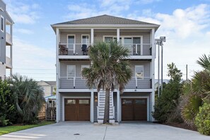 A two-story residential building with a garage, a balcony on the upper floor, and a palm tree in the front yard. - Saltwater Pool | Hot Tub | Steps to Sand (Surf City)