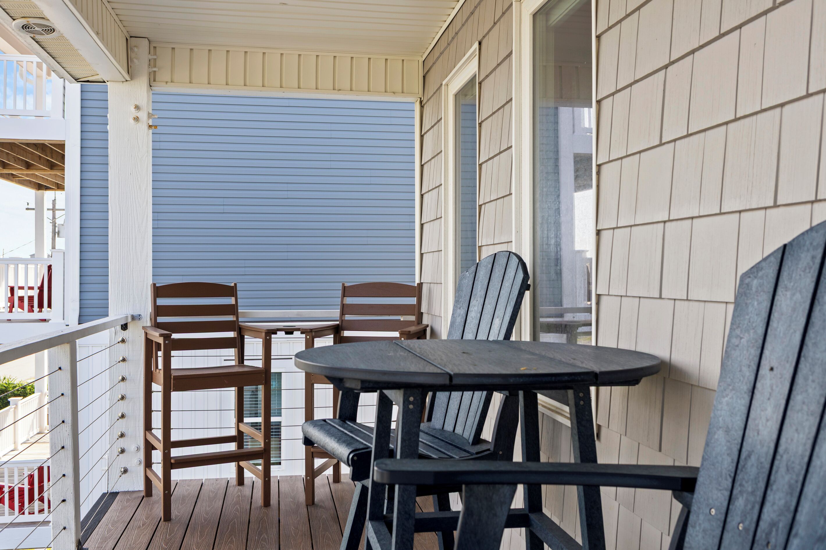 A covered outdoor seating area with two wooden chairs and a table, a white railing, and a blue sliding door.