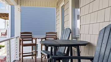 A covered outdoor seating area with two wooden chairs and a table, a white railing, and a blue sliding door.