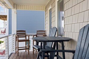 Un espace extérieur abrité, aménagé avec deux chaises en bois et une table, une rambarde blanche et une porte coulissante bleue.