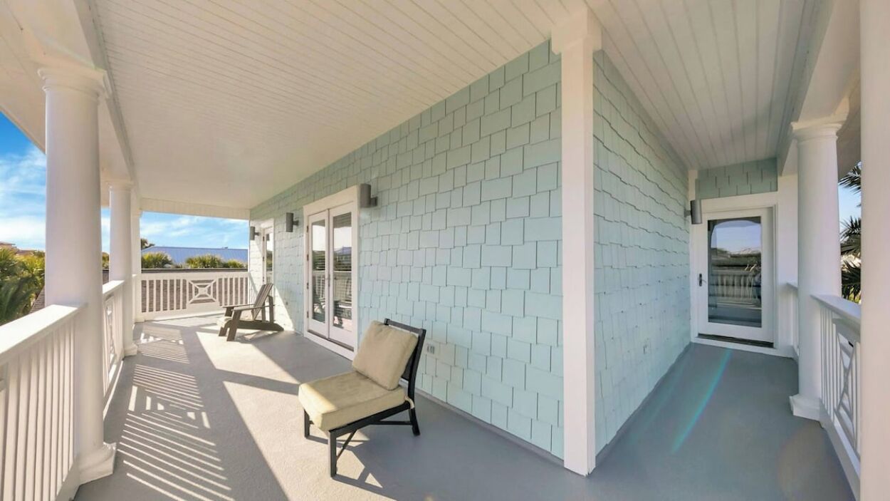 A covered porch with a light blue tiled wall, a white railing, and a single beige chair.