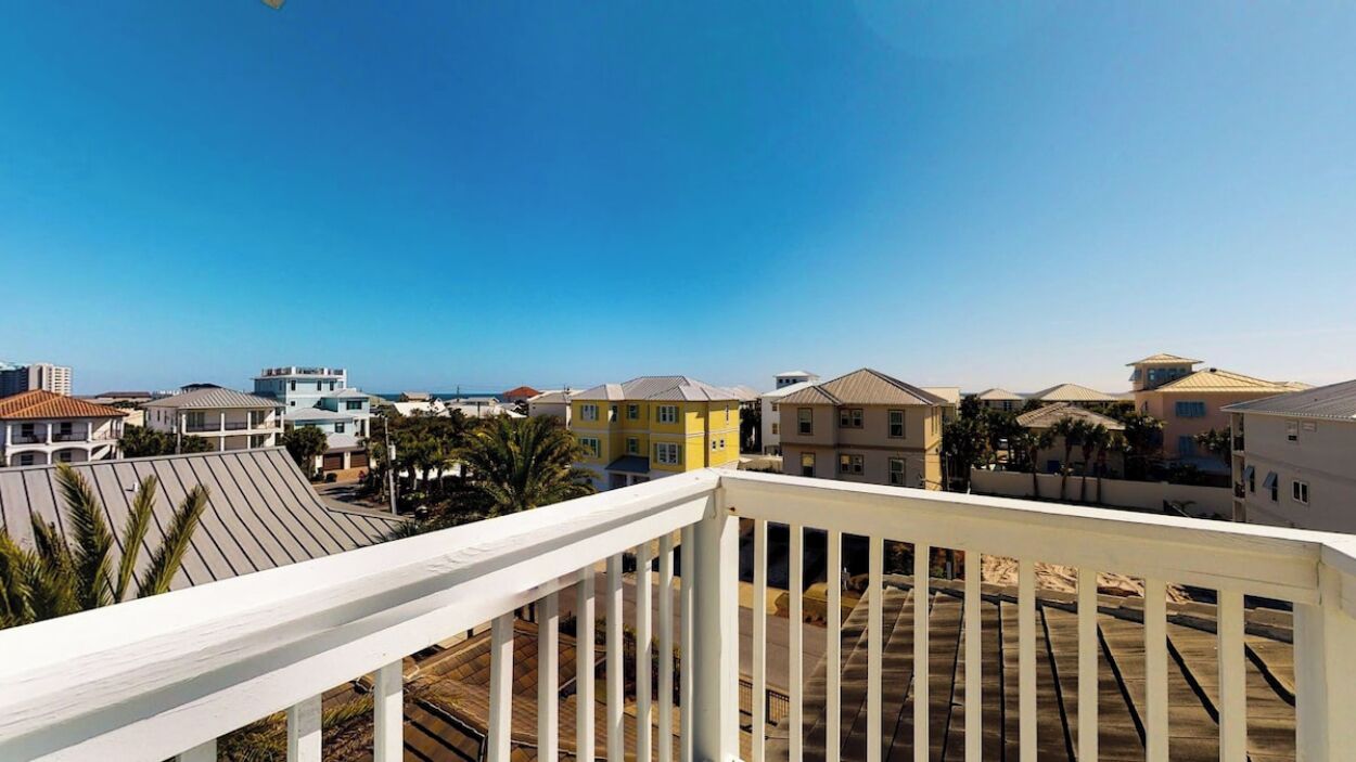 Zona residencial con vista despejada al océano, con casas de diversos estilos de techo y barandilla de balcón blanca.