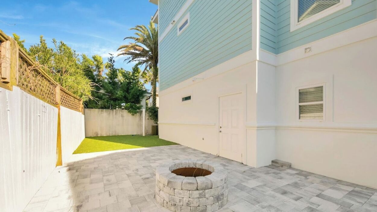 Un patio con un hogar de piedra, una cerca blanca y un edificio azul con garaje.