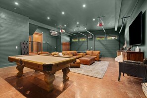Een pooltafel in een kamer met een groene muur, een bank en een televisie.