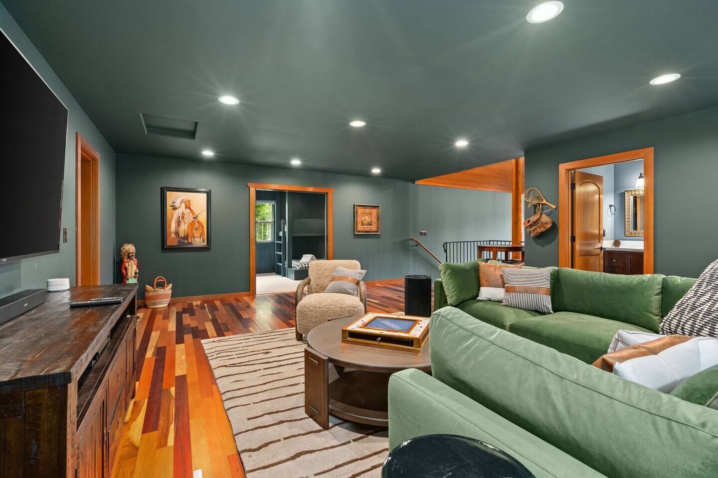 A living room with a green sofa, a wooden coffee table, and a television. There is a patterned rug on the floor and a painting on the wall.