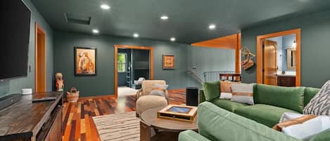 A living room with a green sofa, a wooden coffee table, and a television. There is a patterned rug on the floor and a painting on the wall.