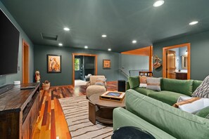 Un soggiorno con un divano verde, un tavolino in legno e una televisione. Sul pavimento c'è un tappeto decorato e al muro un quadro.