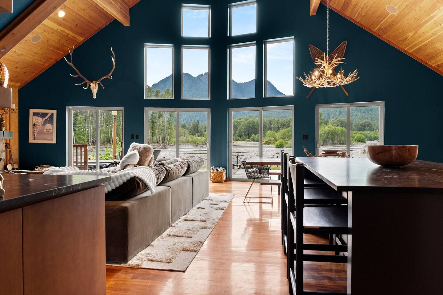 A cozy interior with a large window overlooking a mountainous landscape, a wooden ceiling, and a dining area with a large bowl on the counter.