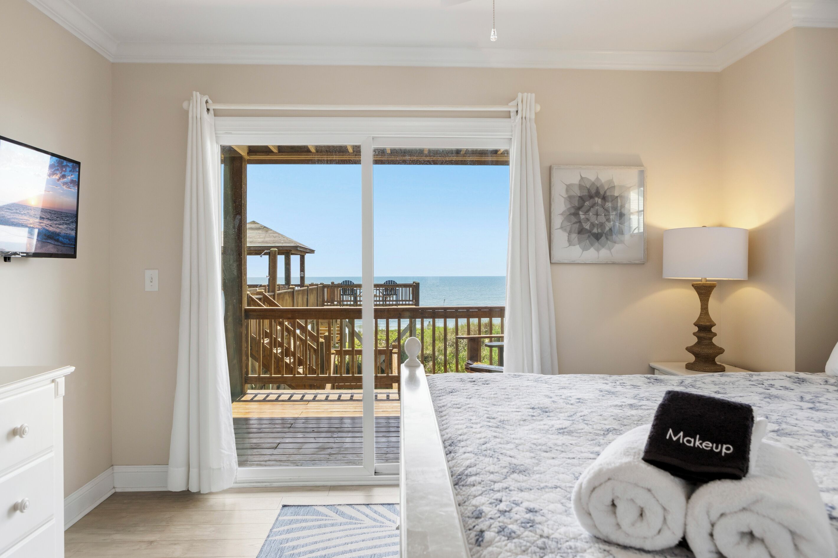 A hotel room with a bed, a TV, a balcony with a view of the sea, and a painting on the wall.