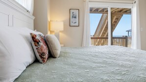 Quarto com cama, luminária de cabeceira, quadro emoldurado e vista para uma varanda com grades de madeira.