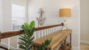 Um banco de madeira com grade branca, uma luminária fixada na parede e uma âncora decorativa.