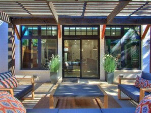 Un espacio al aire libre con dos sofás y una mesa, un acceso por puerta de vidrio y plantas en macetas.