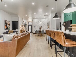 Una cocina moderna con zona de comedor, que incluye una isla central, taburetes de bar e iluminación colgante.