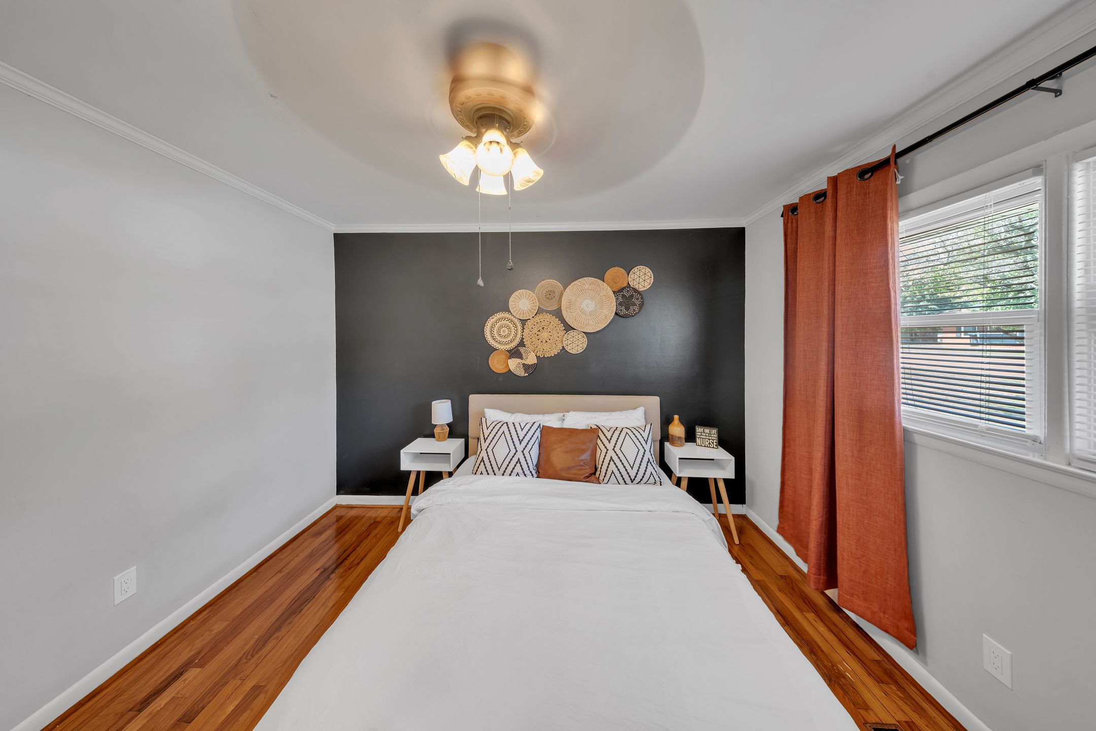 A bedroom with a bed, bedside tables, a wall-mounted light fixture, and a window with curtains.