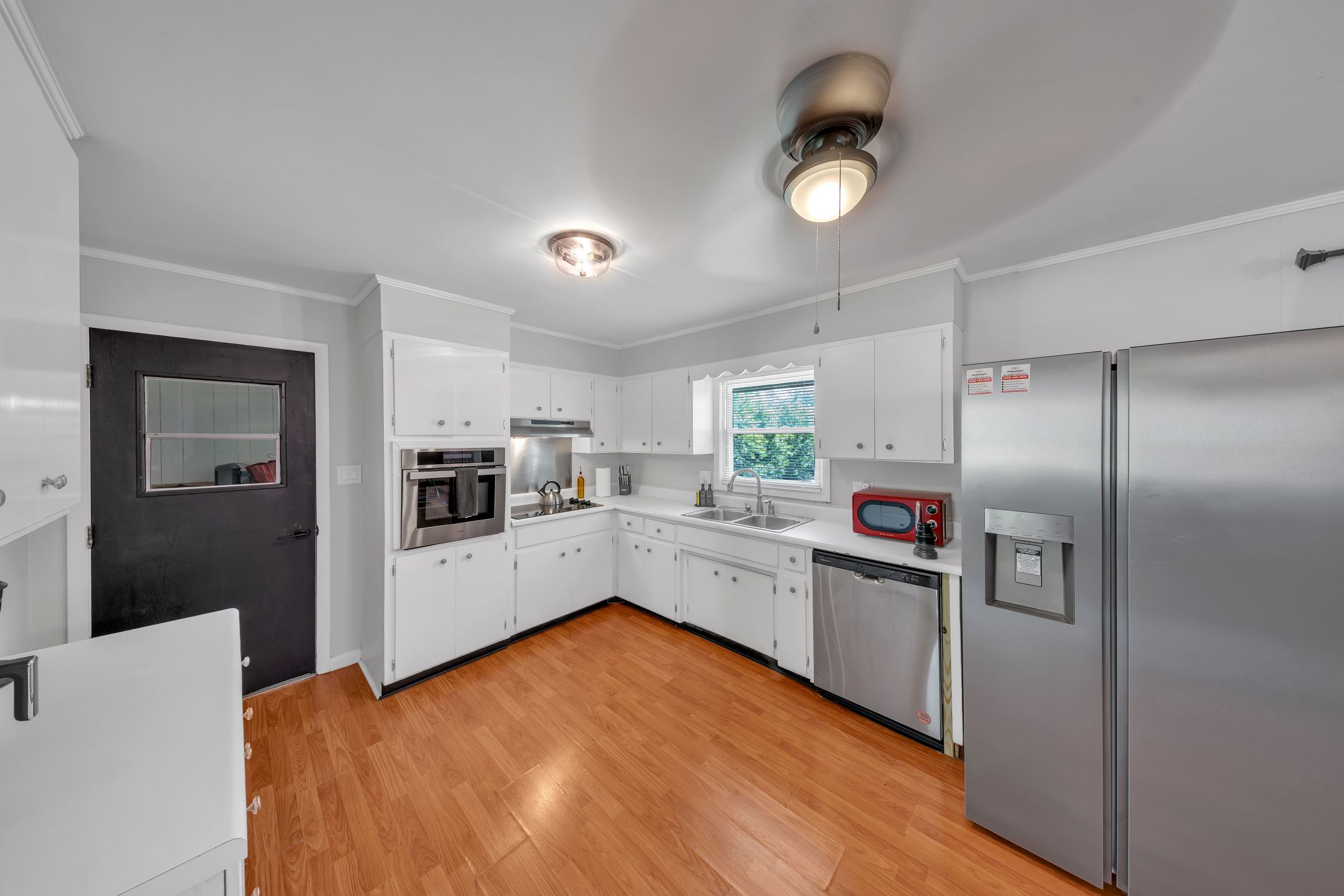 A modern kitchen with white cabinetry, stainless steel appliances, and a wooden floor.