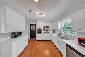 A modern kitchen with white cabinets, stainless steel appliances, and a wooden floor. - The Peach Haus ~ Groovy Stay With Screened Porch (Tifton)