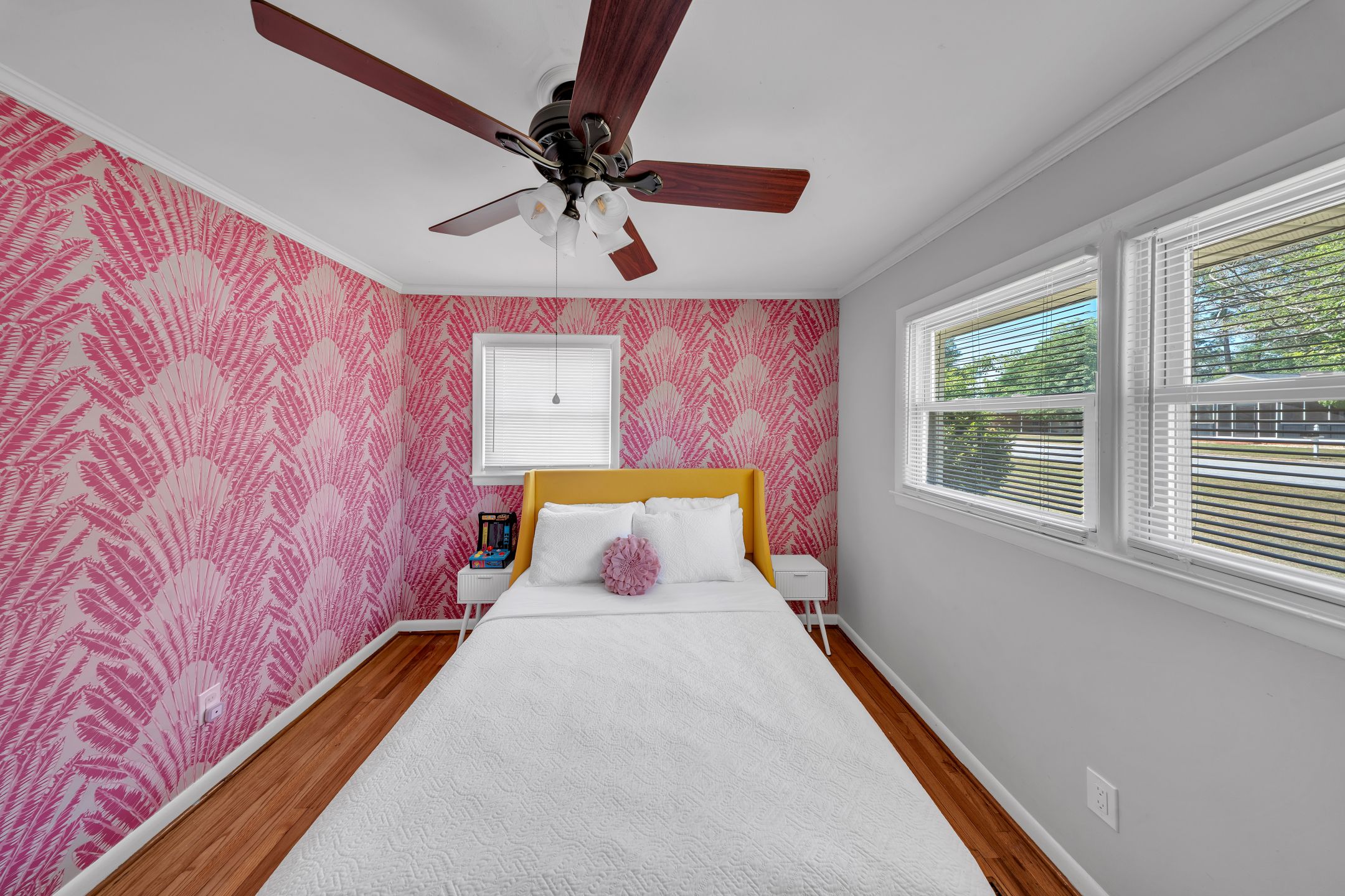 A bedroom with a bed, a ceiling fan, a window with blinds, and a wall with a fern leaf pattern.