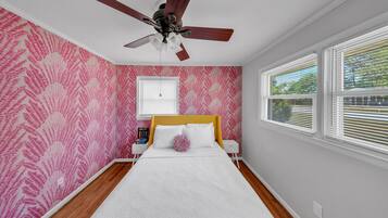 A bedroom with a bed, a ceiling fan, a window with blinds, and a wall with a fern leaf pattern.