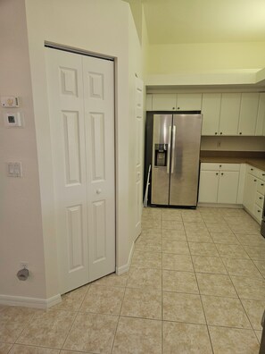 A kitchen with white cabinets, a stainless steel refrigerator, and a tiled floor. - The Brooks 2 Bedroom +den condo at Lighthouse Bay A Perfect Retreat (Bonita Springs)