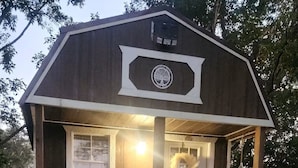 A small wooden cabin with a porch, two Adirondack chairs, a fire pit, and a welcome sign. - The Dasher Den is a Cozy Tiny Cabin located right off of Highway 41 (Valdosta)