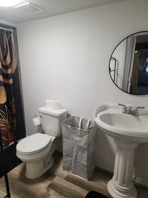 A bathroom with a toilet, a white sink, and a striped trash bin.